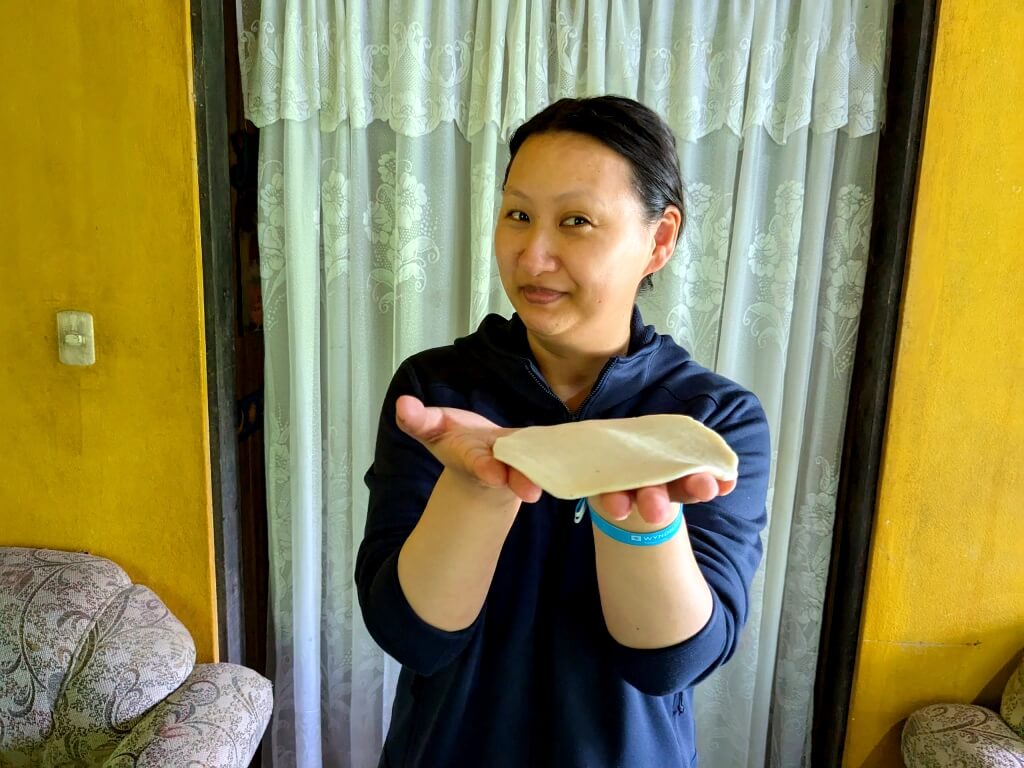 Tourist showing her freshly made corn tortilla during a cooking class in a cozy Costa Rican home.