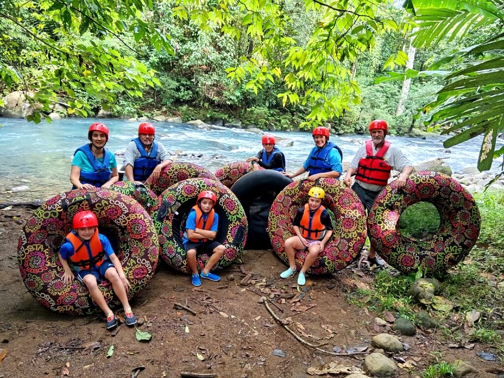 Family of excited tourists pose for a photo before tubing down the turquoise Rio Celeste River, surrounded by lush rainforest.