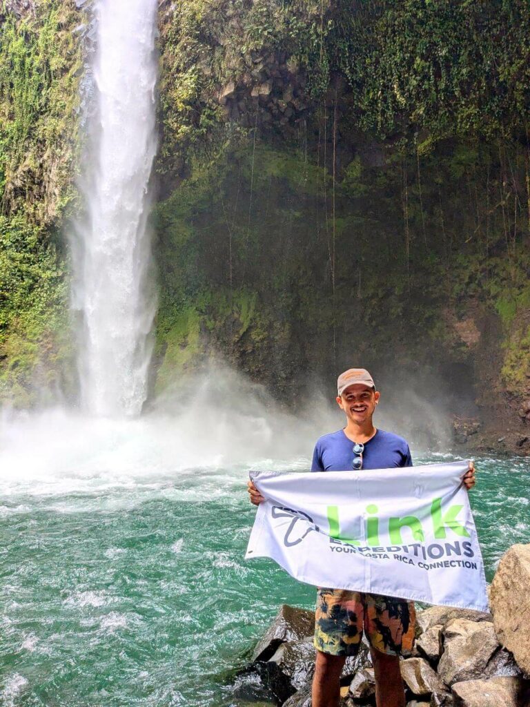 Alberto Salas, founder of LINK Expeditions Travel Costa Rica, holding the Link Expeditions flag at La Fortuna Waterfall.