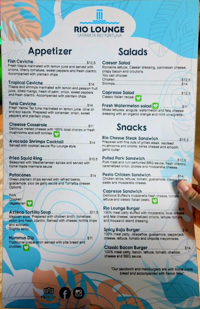 Food menu at Rio Lounge restaurant near La Fortuna Waterfall entrance, highlighting appetizers, salads, and snacks.