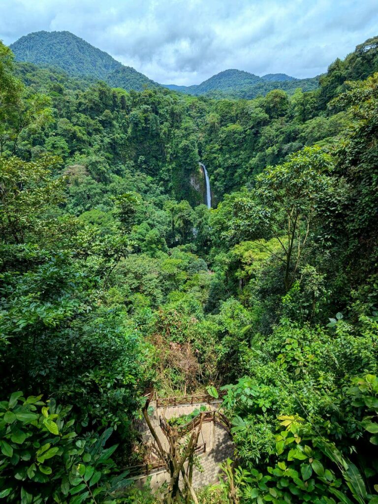 Vertical view of La Fortuna Preserve with La Fortuna Waterfall, mountains in the background, and the trail winding down the canyon.