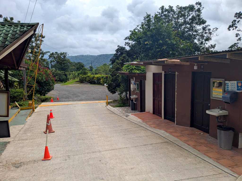 Entrance to the property with visible signage and nearby bathroom facilities at the base of Arenal Volcano.