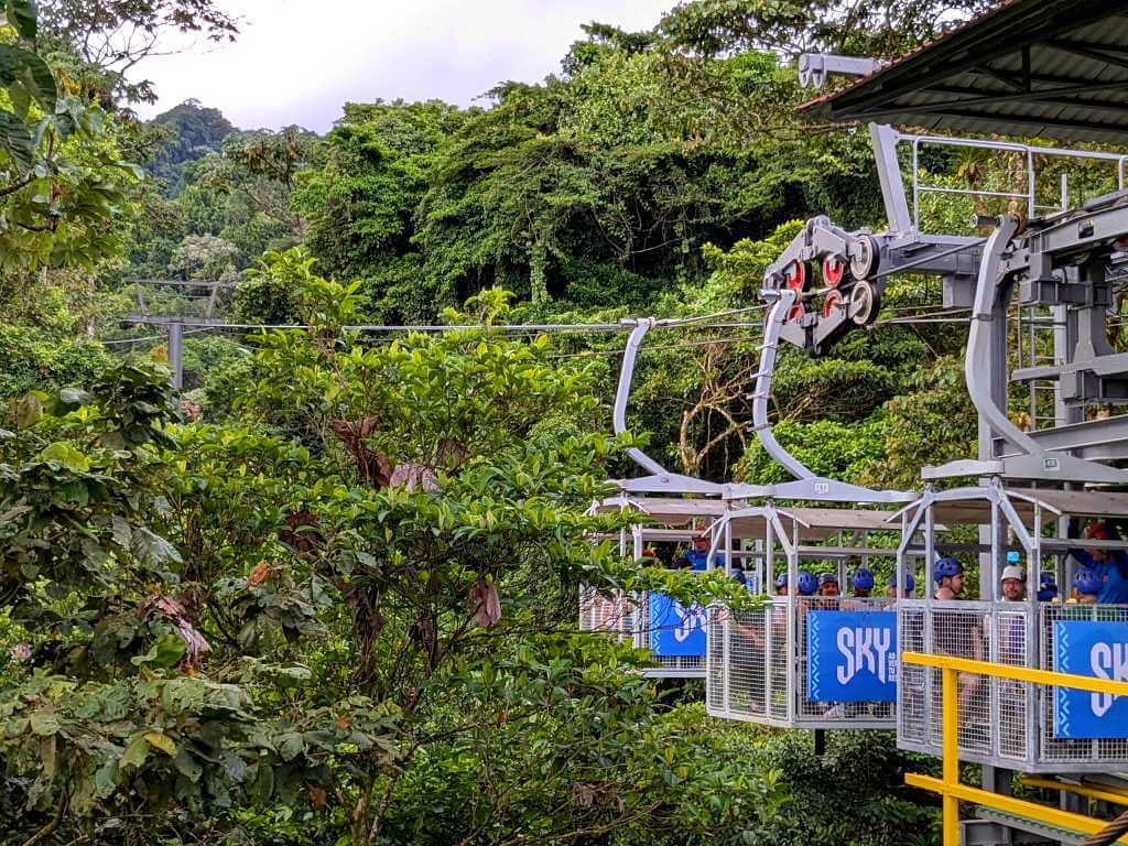 Three tram carts carrying travelers equipped for ziplining, ascending the mountain.