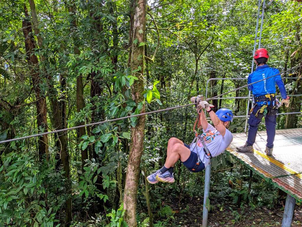 Person gliding down the zipline in proper position, holding the pulley and wearing full safety gear.