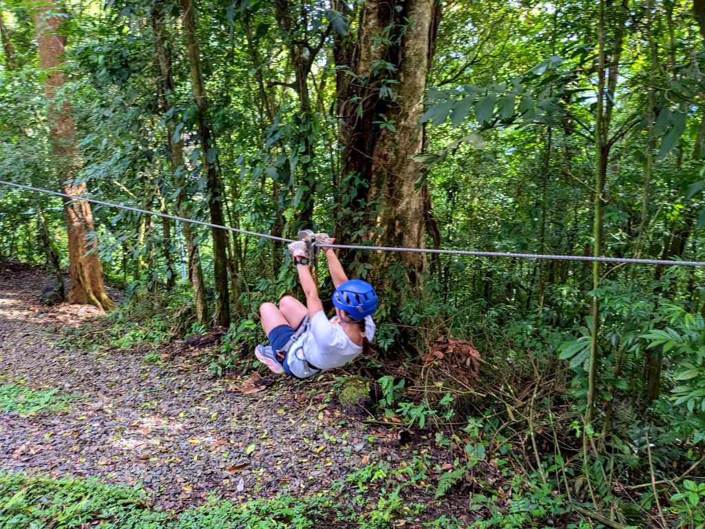 Person practicing on the first, shorter zipline while wearing full safety gear, including a helmet and gloves.