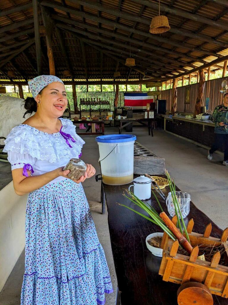 Costa Rican woman dressed in traditional attire, holding a tapa de dulce and explaining its cultural significance.