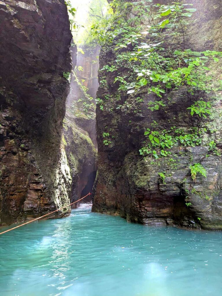 Tall vertical rocks forming a narrow canyon along Rio Blanco, with blue pools and a rope for swimming assistance.