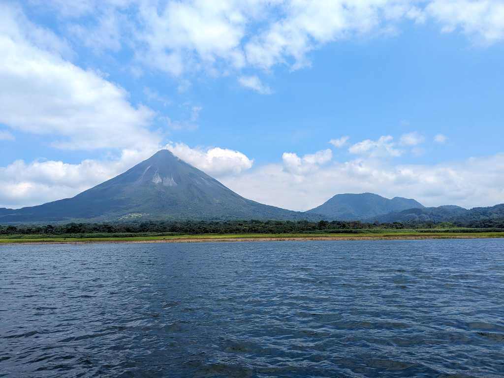 Stunning view of Arenal Lake with intense blue waters, mountains, and light blue skies taken from a boat on a sunny day.