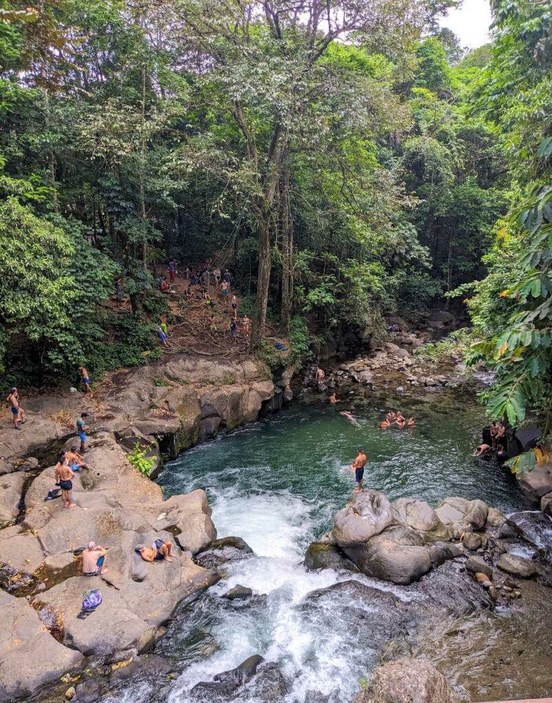 People swimming and jumping in the natural river pool at El Salto, Arenal River, a popular but unregulated spot with no lifeguards.