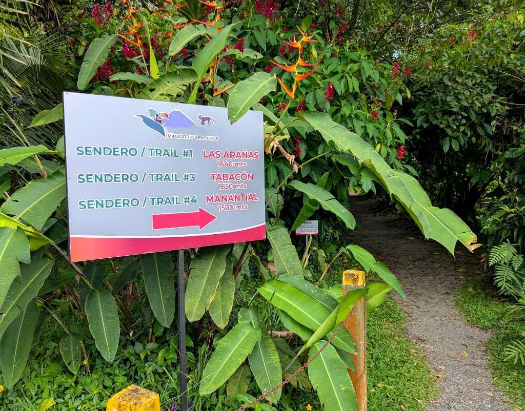 Entrance to rainforest trails at Arenal Volcano with sign and lush plants on both sides.