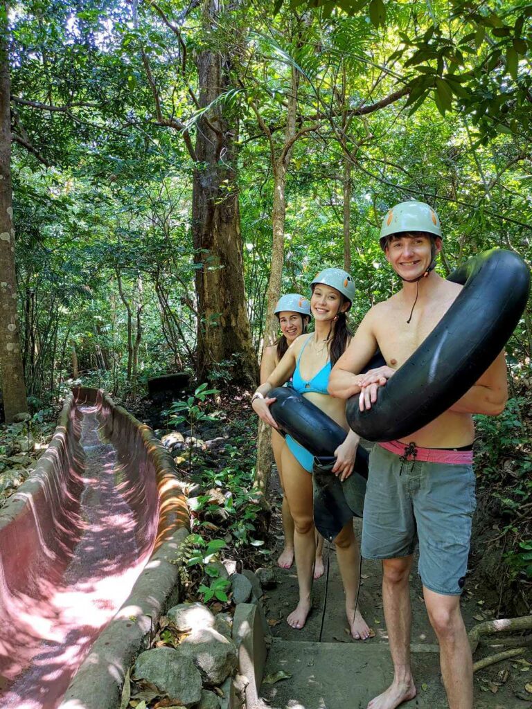 Travelers carrying innertubes and wearing helmets as they walk up the trail to the start of the water slide at Buena Vista del Rincón.