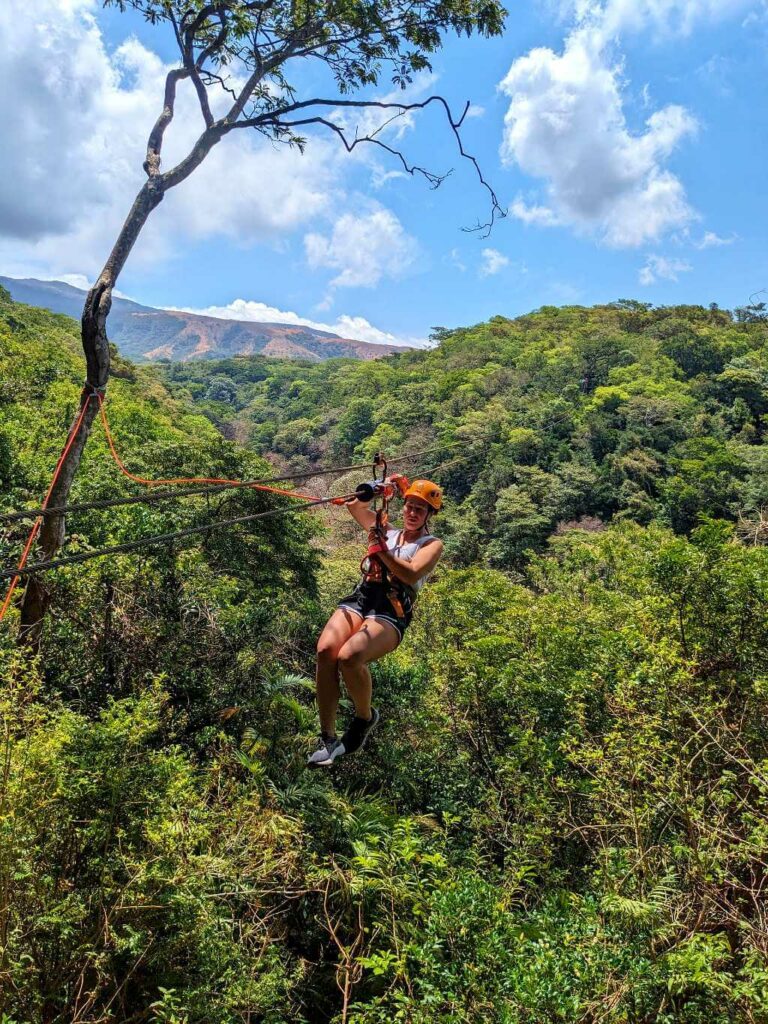 Traveler approaching a zipline platform on a tree with Rincón de La Vieja mountains in the background on a sunny day.