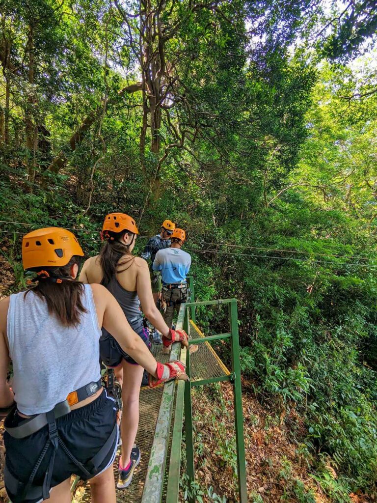 Travelers lining up for the next zipline at Buena Vista del Rincón, wearing helmets, gloves, and harnesses.