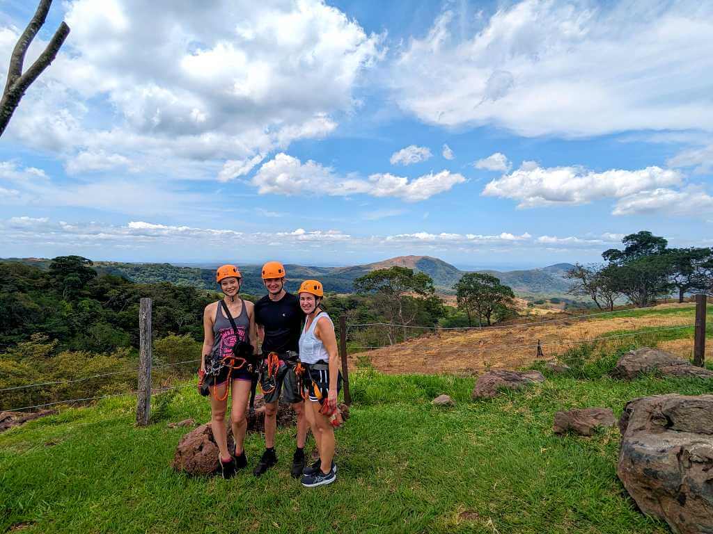 Travelers posing at the end of the ziplining experience with views of grass fields, hills, and La Pampa in Guanacaste, Costa Rica.