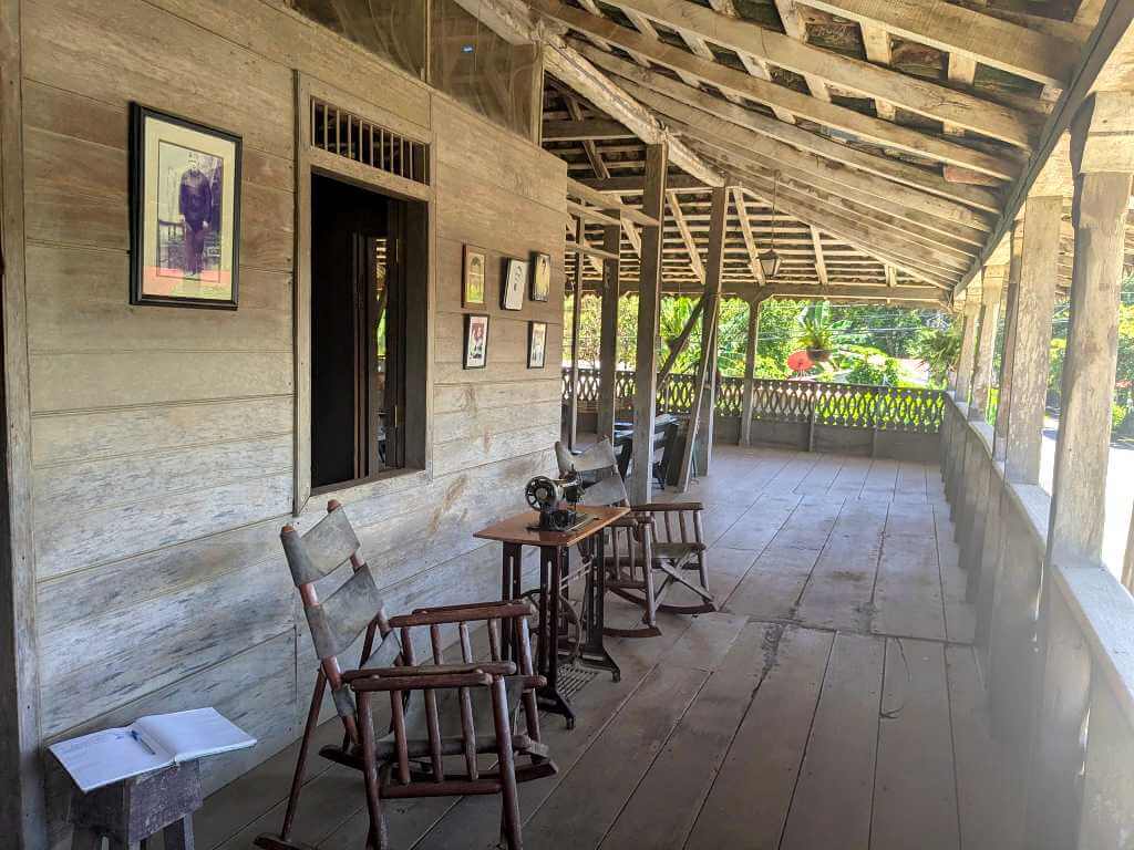 Corridor of a rustic Guanacaste house with wooden chairs, benches, and an antique sewing machine.