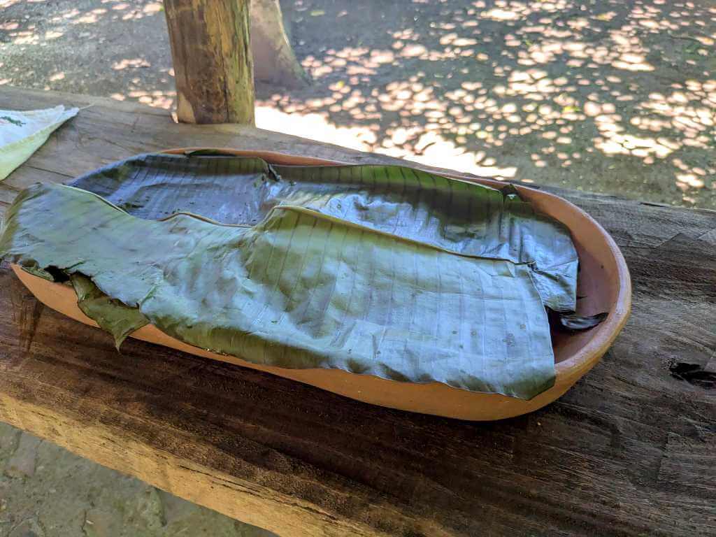 A wooden platter covered with plantain leaves, holding freshly made corn tortillas